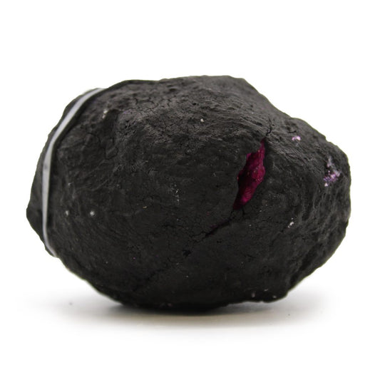 A dark, roughly spherical rock rests, showing a small crevice exposing purple crystals within, against a plain white background.