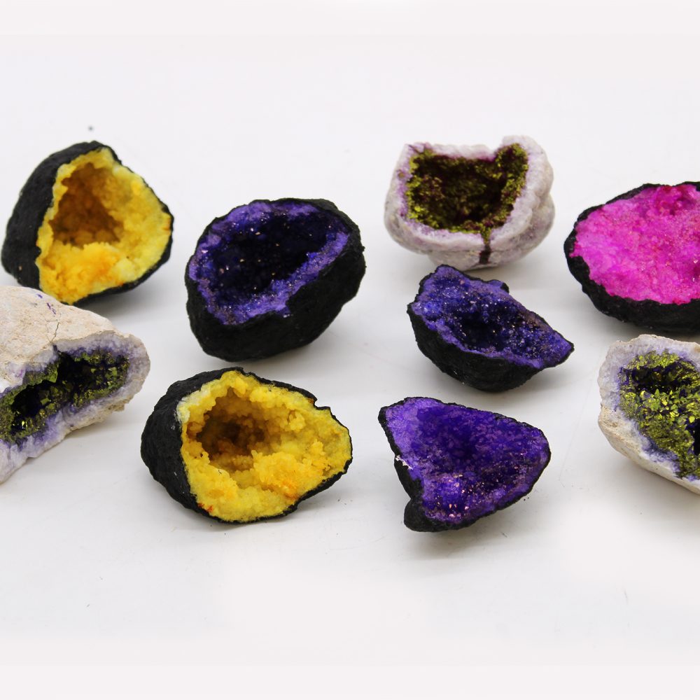 Geode halves, in purple, yellow, green, and pink, sit open-faced, showing crystal insides. The geodes are arranged on a white surface.