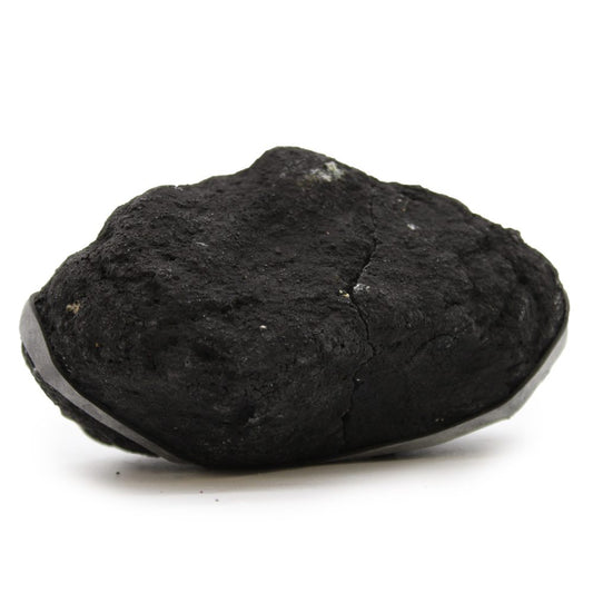A chunk of rough, black charcoal sits at rest against a plain, white background. A piece of metal is attached to the left of the charcoal.