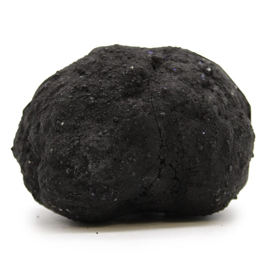 A large, roughly spherical, black clod rests on a white surface, casting a small shadow. Its surface is uneven and textured with some slight purple sheen.