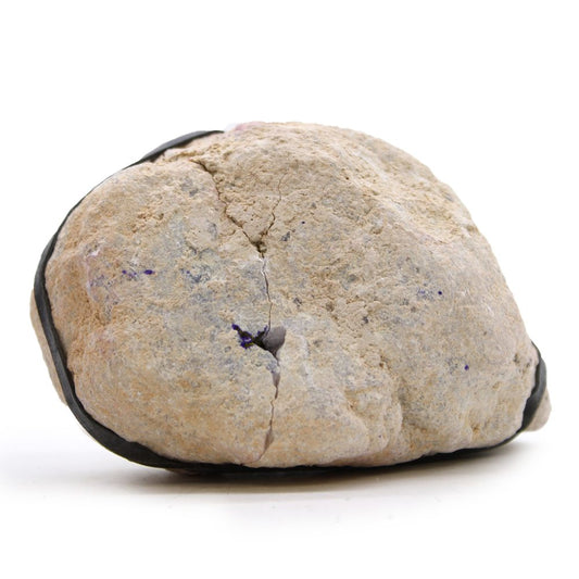 A tan, rough rock sits on a white surface. A black rubber band is wrapped around it, holding a crack together. Small patches of purple are scattered on its surface.
