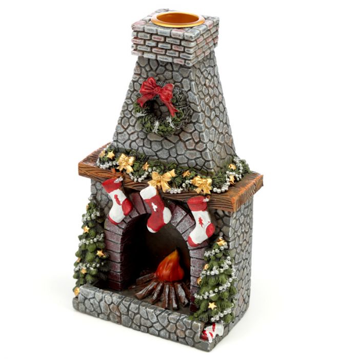 A miniature stone fireplace adorned with a wreath, festive garlands, and red stockings; a small fire burns inside, surrounded by pine trees, creating a holiday atmosphere.