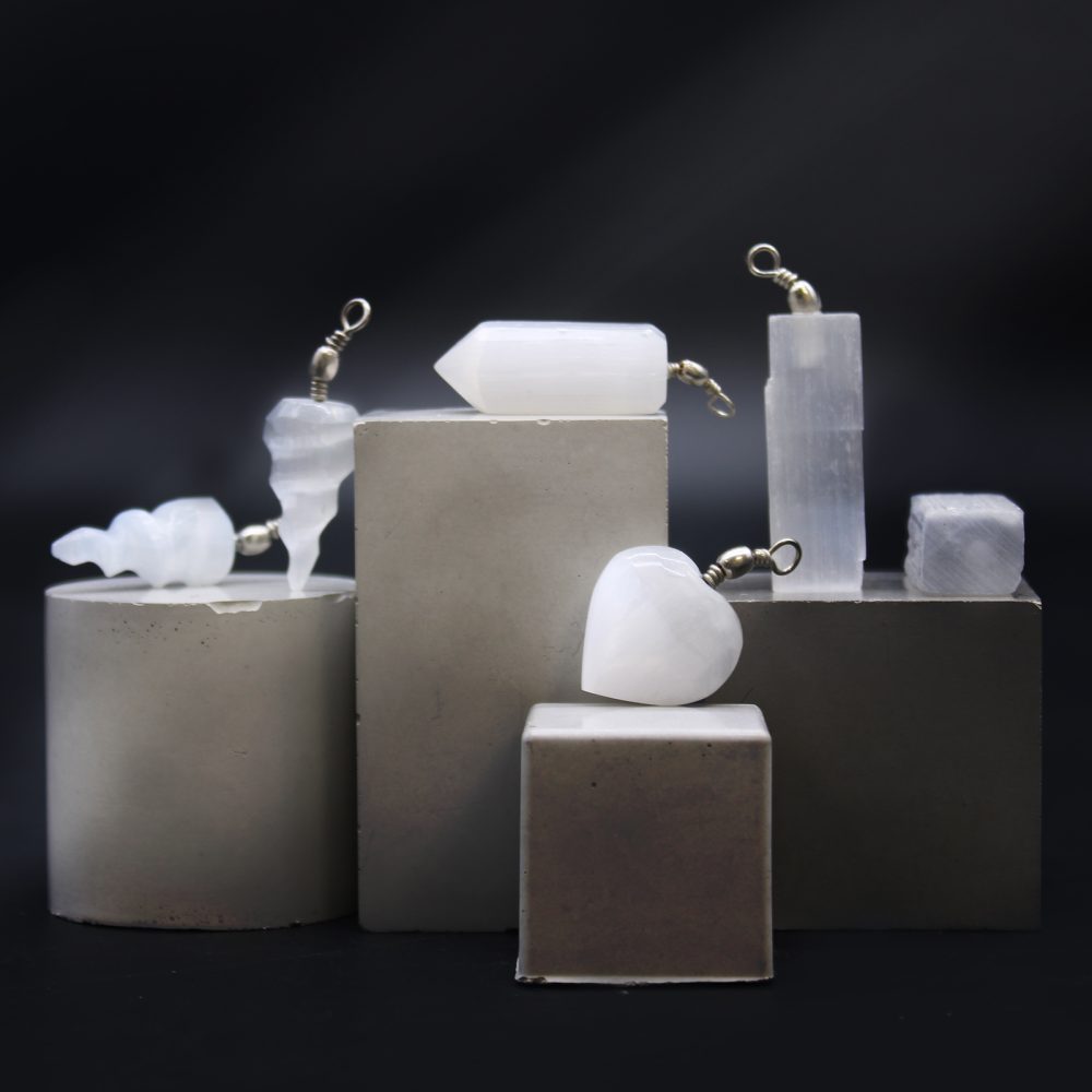Assorted white crystal pendants sit atop varied gray geometric blocks against a black background, creating a layered and textured display.