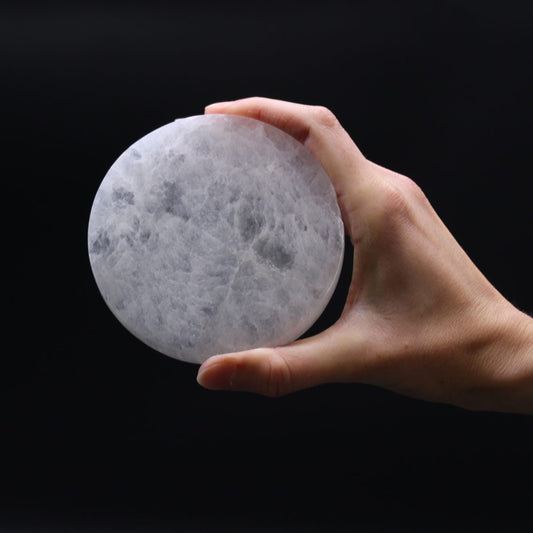 A hand holds a cloudy, white, stone orb, fingers slightly curved around its surface, in front of a black background.