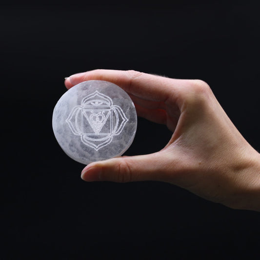 A round, white stone with a chakra symbol engraved on it is being held by a hand, isolated against a plain black background.