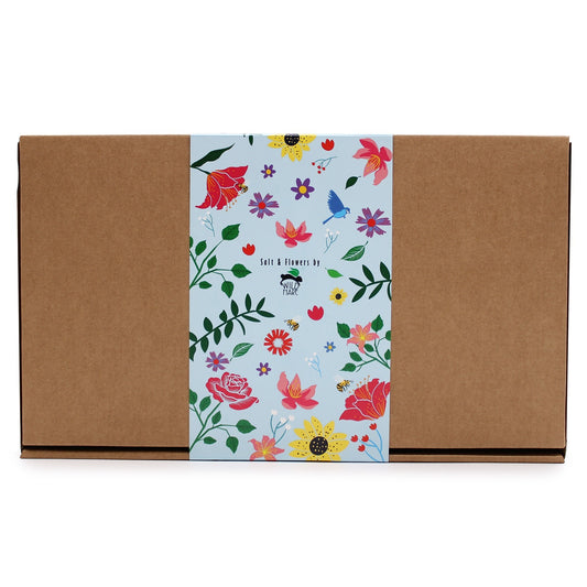 A closed, rectangular, cardboard box has a light blue floral-patterned band wrapped around its center. The band includes the text "Salt & Flowers by WILD HARE."