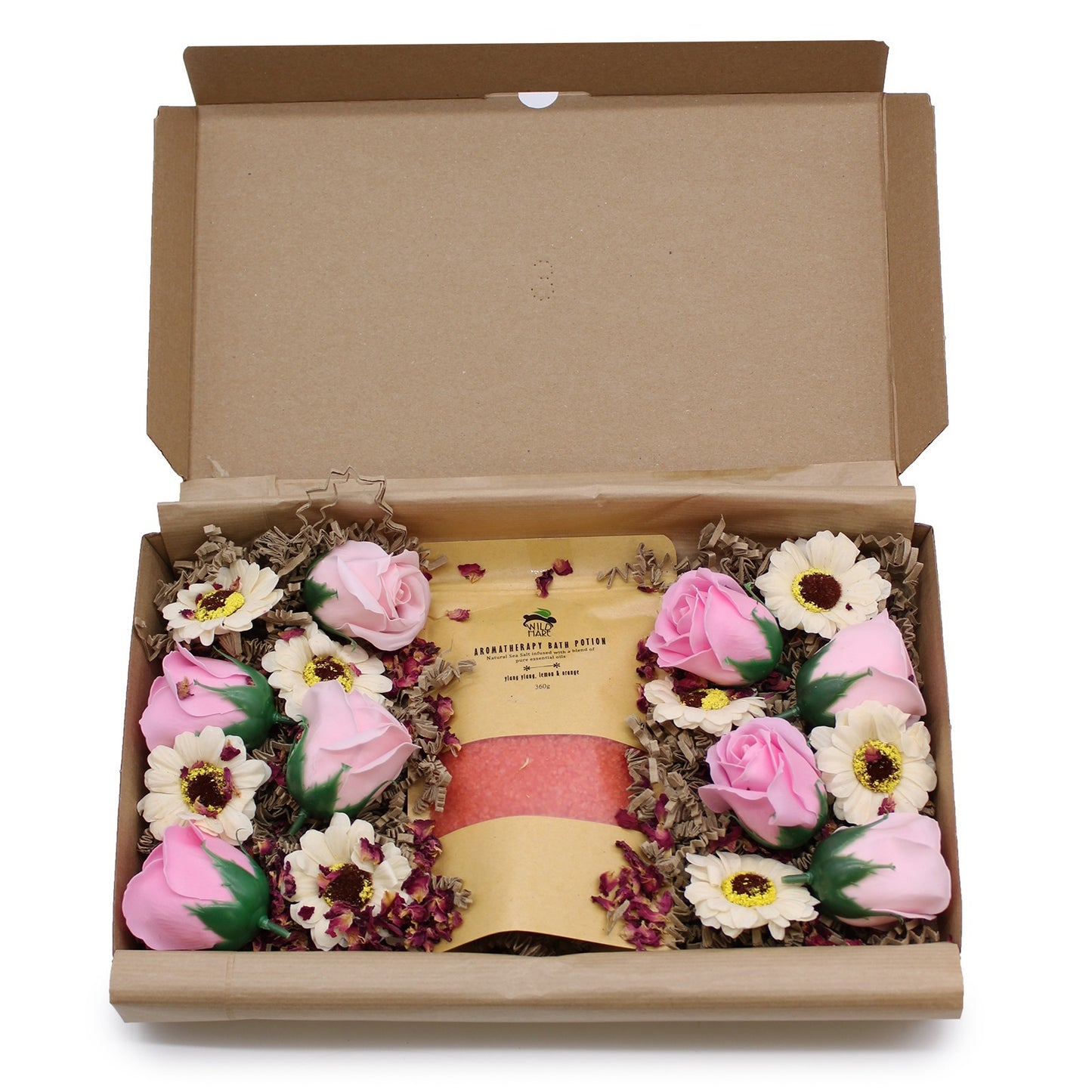 A gift box reveals pink bath salts inside a kraft paper bag labeled "AROMATHERAPY BATH POTION." Decorative roses and daisies surround the bag, nestled on brown shredded paper, inside the cardboard box.