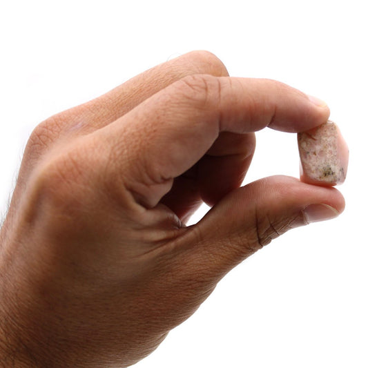 A fair-skinned hand holds a small, rectangular pink stone between the thumb and index finger, against a stark white background.
