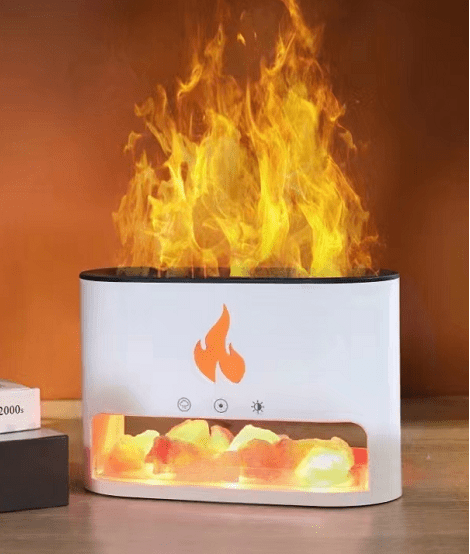 A white, rectangular faux fireplace burns brightly with realistic-looking flames. An orange flame logo is printed on the front of the device, which has three small control icons next to it.