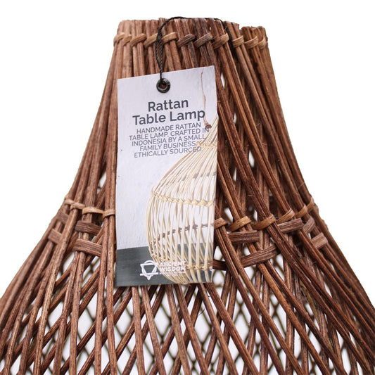 A woven rattan lampshade, displays a tag, sits against a white background. The tag describes it as a handmade rattan table lamp from Indonesia.