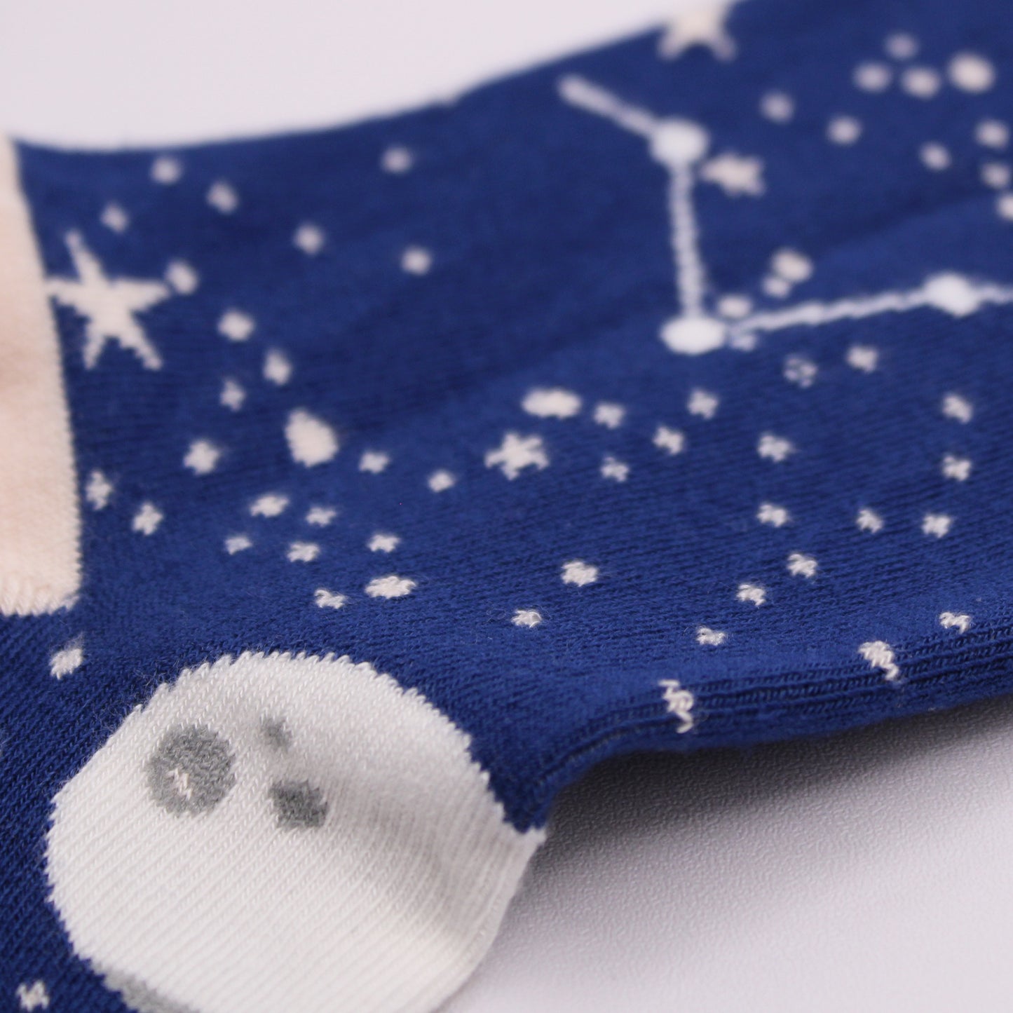 A navy blue sock, featuring a celestial design of stars and constellations, rests on a white surface.