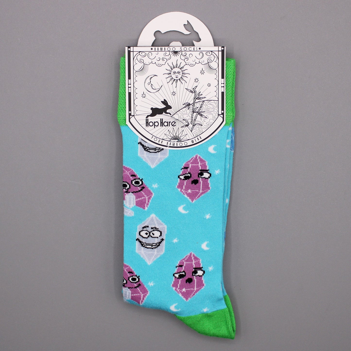 A pair of light blue socks, featuring cartoon crystals, hangs from a tag against a gray background. The tag reads: "*BAMBOO SOCKS* Hop Hare YOUR BAMBOO WEAR".