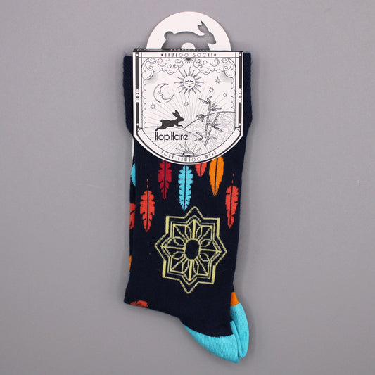 A pair of dark-navy socks, displaying colorful feather and geometric patterns, hangs from its packaging against a gray backdrop. The packaging features the text: "*BAMBOO SOCKS*", "Hop Hare", "YOUR BAMBOO WEAR".