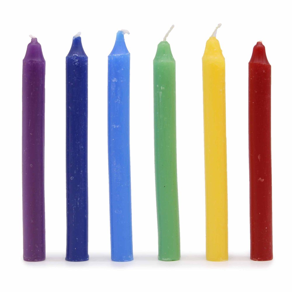 Six short candles stand upright, displaying the colors purple, blue, light blue, green, yellow and red, in a row against a white background.