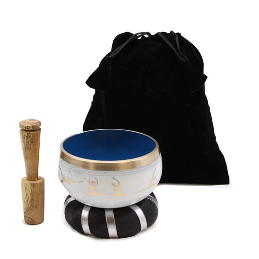 A singing bowl set includes a blue-interior bowl on a black cushion, a wooden mallet beside it, and a black drawstring bag in the background.