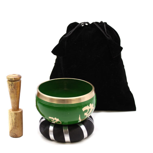 A green singing bowl with gold accents sits on a black, striped cushion. Nearby, a wooden mallet rests upright. Behind them, a black drawstring bag is visible.