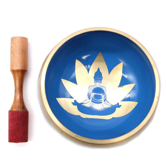 A blue singing bowl features a gold design of a meditating figure on a lotus, accompanied by a wooden mallet with a red felt end, placed on a white surface.