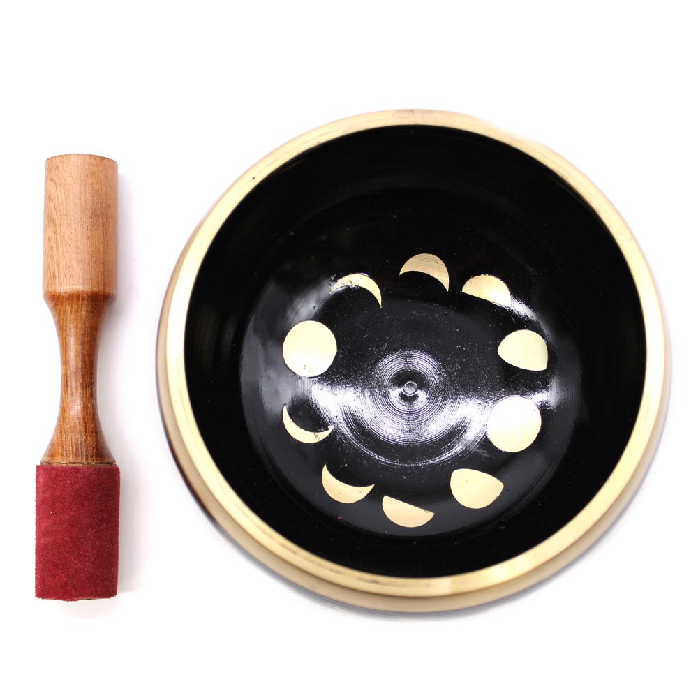 A black singing bowl with gold phase designs sits beside a wooden mallet with a red felt covering, placed on a white surface.