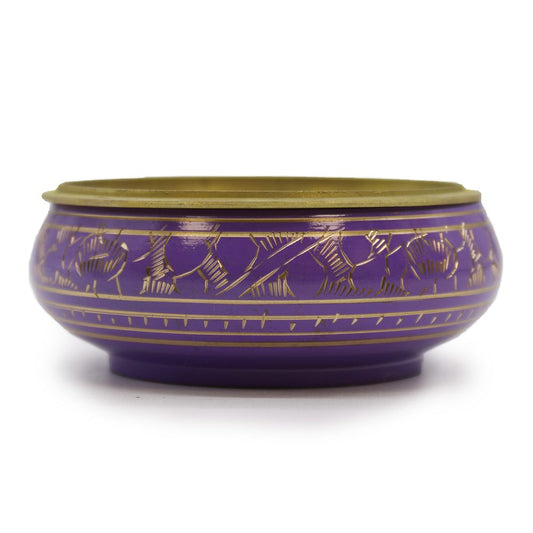 A round, purple bowl with intricate gold patterns sits on a white surface. The bowl has a golden rim and features decorative linear motifs encircling its exterior.