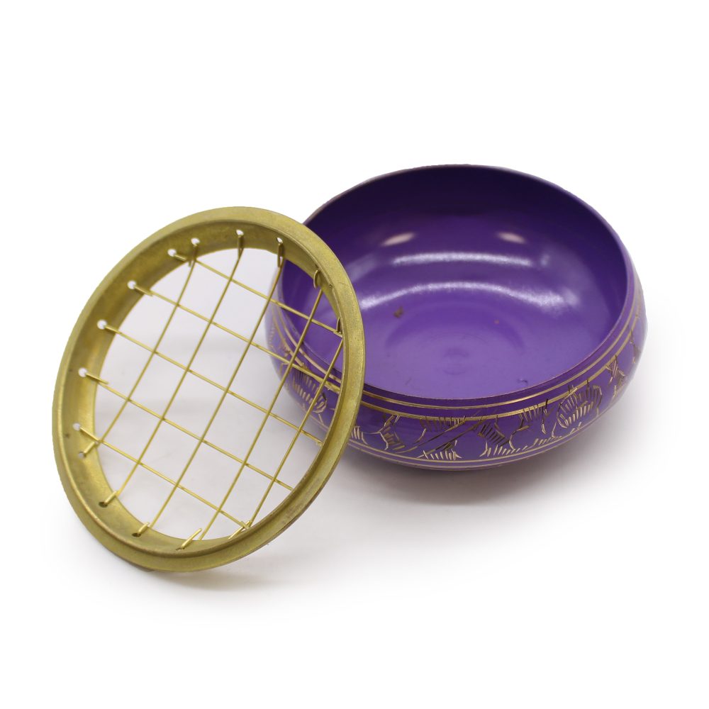 A purple singing bowl with golden engravings sits open beside a detached golden grid lid, placed on a white surface.