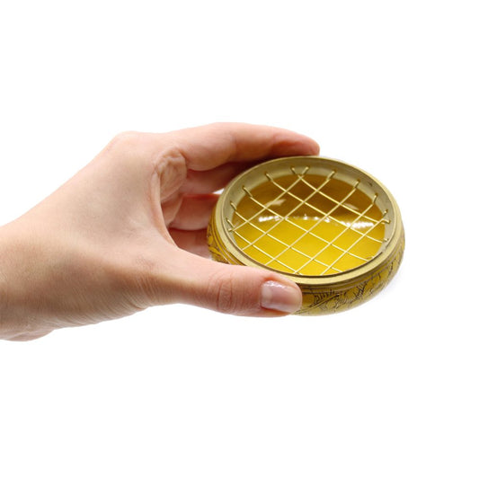 A round, patterned yellow bowl with a lattice lid is held between fingertips against a plain white background.