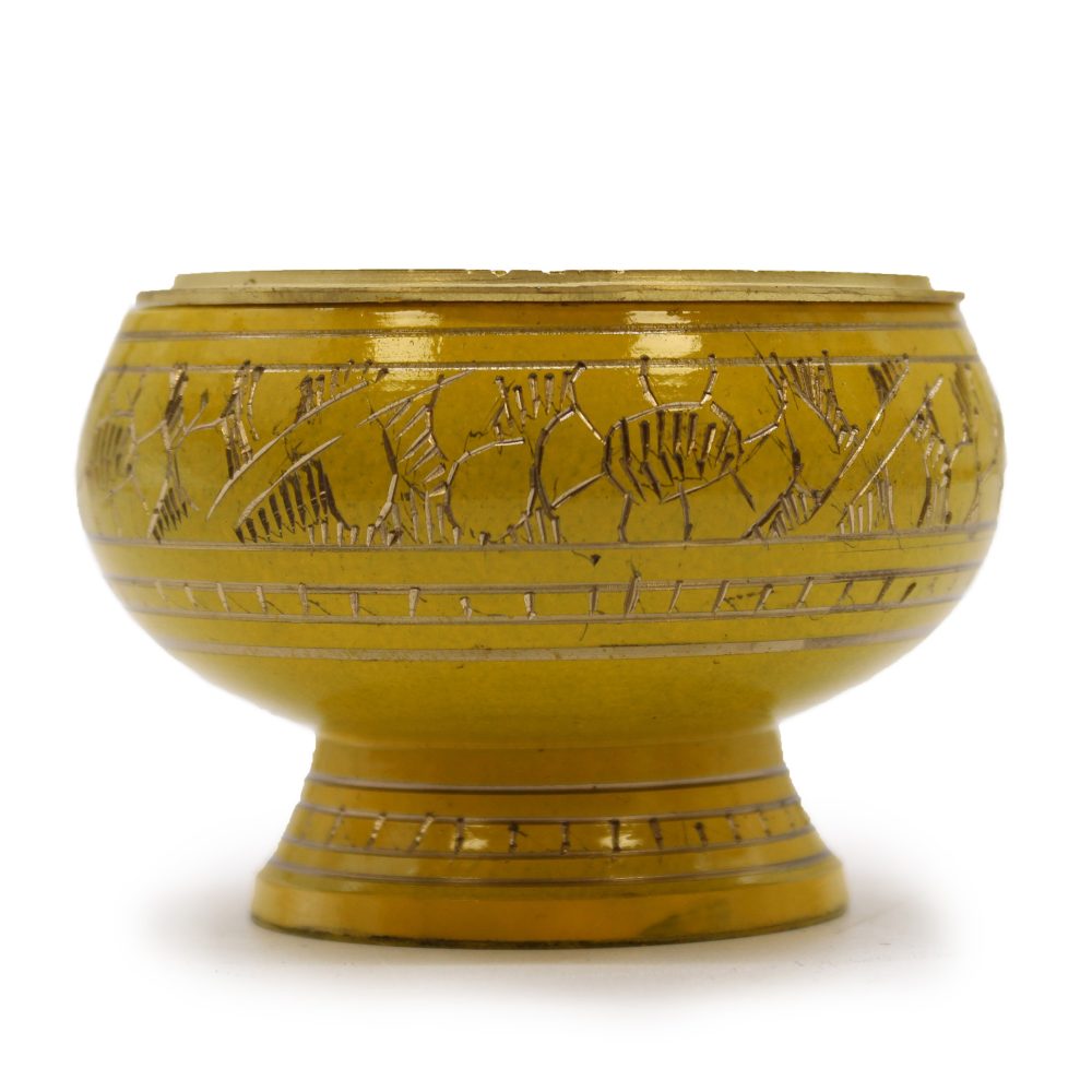 A round, yellow ceramic bowl features intricate engraved floral patterns. It rests on a short pedestal, creating a raised base, and sits against a plain white background.