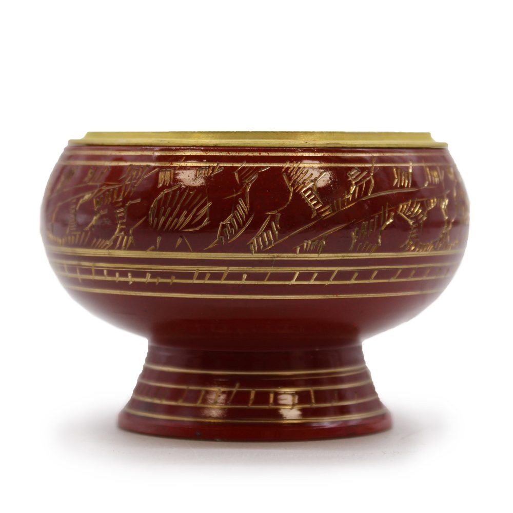 A red, decorative lacquer bowl rests on a pedestal, featuring gold engraved patterns of leaves. The bowl is shown against a plain white background.