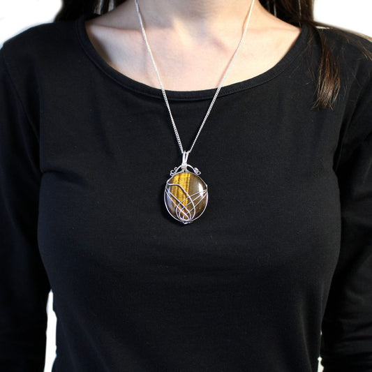 A tiger's eye pendant hangs from a silver chain on a person with long dark hair wearing a black shirt.