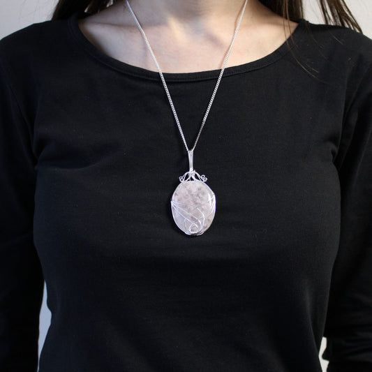 A stone pendant dangles on a silver chain against a black long-sleeved shirt. The oval stone is wrapped with silver wire in a looping design.