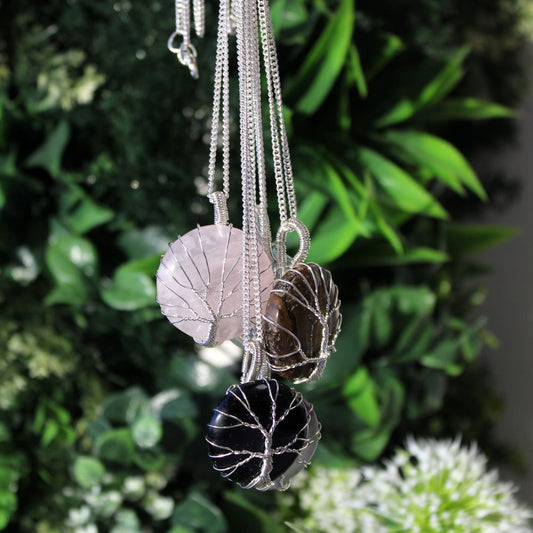 Three crystal pendants hang, each wrapped in silver wire to resemble a tree, against a green foliage background.