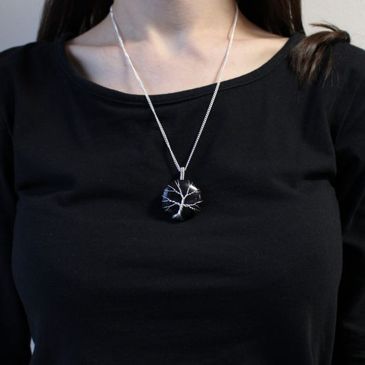 A necklace hangs on a woman wearing a black top. The pendant is a black, round stone with silver wire forming a tree.