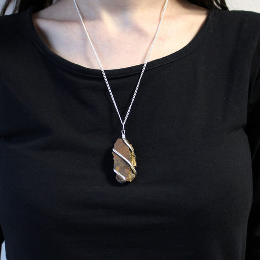 A brown, rock pendant wrapped with silver wire hangs from a silver chain around a woman's neck. She wears a black shirt.