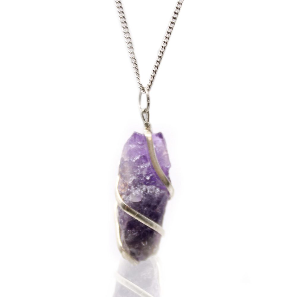 A raw, purple amethyst crystal, wrapped in silver wire, dangles from a silver chain against a stark white background.