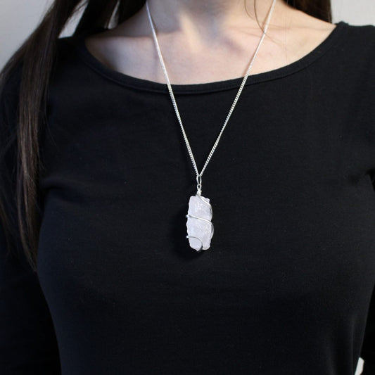 A woman wearing a black top has a raw clear crystal pendant that hangs from a silver chain resting on her chest.