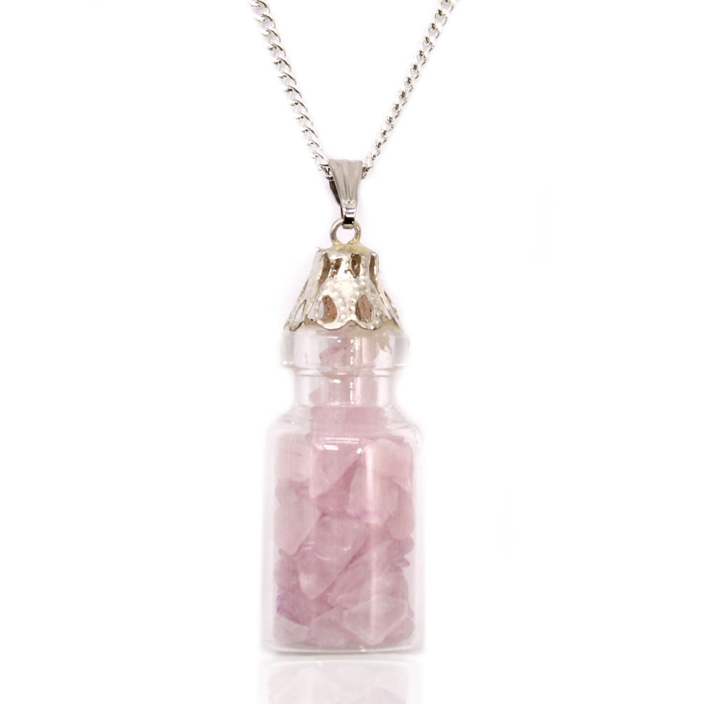 A clear glass bottle pendant hangs from a silver chain. Inside, small, light pink, rough-cut gemstones are visible. The pendant and chain sit on a white surface.