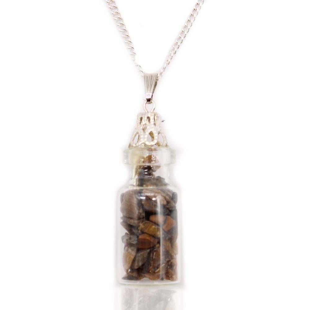 A small glass bottle necklace holds brown crystal shards, presented on a white surface with a reflection underneath. The necklace chain is silver.