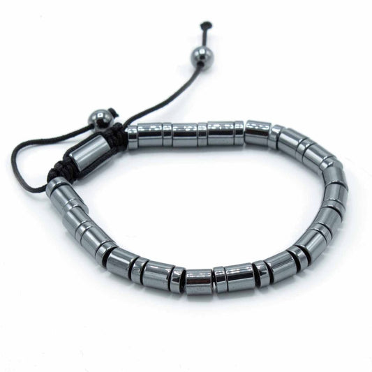 A bracelet, composed of cylindrical, metallic hematite beads, sits curved and adjustable with a black cord and beads against a stark white background.