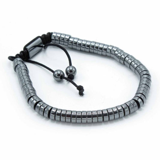 A bracelet of short, metallic grey cylinders lies curved on a white surface. Black cords and two small metallic spheres hang from the bracelet's ends.