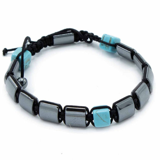 A bracelet lies coiled on a white surface. Alternating square beads of turquoise and grey are strung together with black cord to make the bracelet.