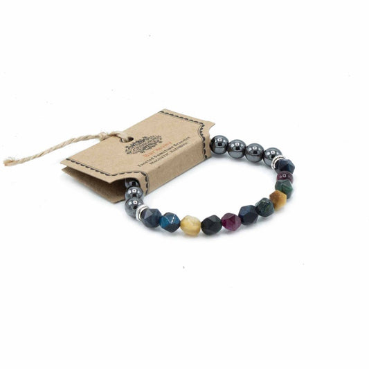 A bracelet with alternating hematite beads and faceted gemstone beads lies next to its rectangular tag labeled, “Accessory Harmony Faceted Gemstone Bracelet MAGNETIC RAINBOW" on a white surface.