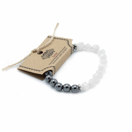 A bracelet lies with its tag on a white surface. The tag reads: "Accessories. Love. Faceted Gemstone Bracelet. Magnetic Rose Quartz." The bracelet has metallic beads and white geometric beads.