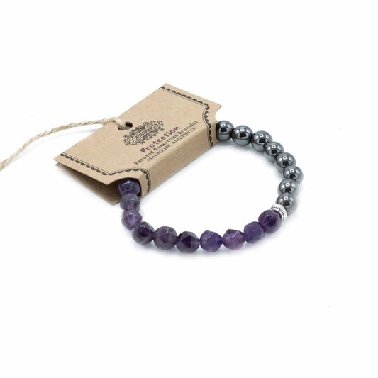 A beaded bracelet circles near its tag, which reads “Protection Faceted Gemstone Bracelet MAGNETIC AMETHYST.” The bracelet features purple gemstones near the tag and gray ones further away. It lies on a white surface.