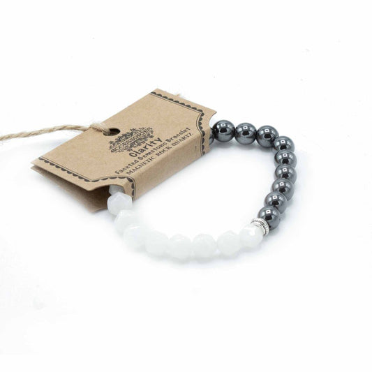 A stretch bracelet rests on a white surface, half white faceted stones and half shiny black stones. It has a tag that reads “ACCESSORIES, Clarity, Faceted Gemstone Bracelet, MAGNETIC ROCK QUARTZ”.