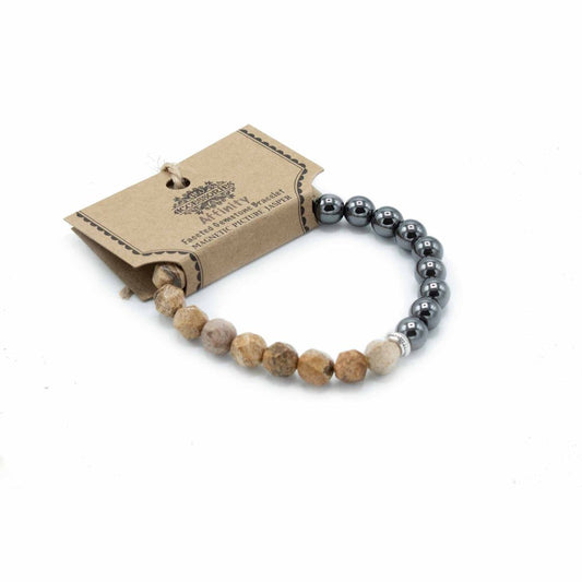 A beaded bracelet, partially looped around its brown tag, is seen against a white background. The tag reads “Accessories, Affinity, Faceted Gemstone Bracelet, MAGNETIC PICTURE JASPER”. The beads are tan and silver colored on one side, with gray metal beads on the other.