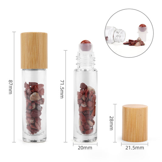 Two clear glass bottles, one with a wooden lid and the other with a rollerball, sit among loose red stones, with a detached lid and measurements overlaid: 87mm, 71.5mm, 20mm, 28mm, 21.5mm.