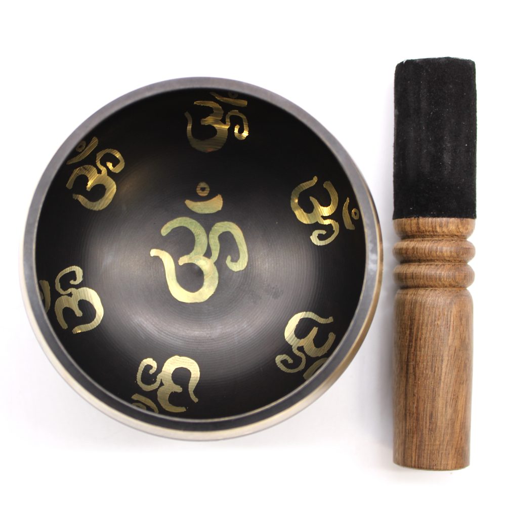 A black singing bowl features golden "Om" symbols inside. It is accompanied by a wooden striker with a suede covering, placed on a white background.