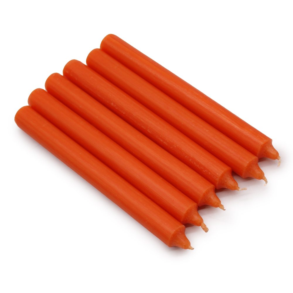 Six orange, unlit, cylindrical candles lay side by side on a plain white surface, with their pointed tips facing the same direction.
