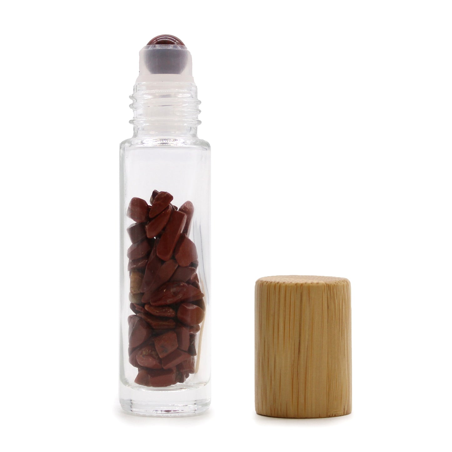 A clear roll-on bottle holds small, jagged red stones. Its lid is beside it, made of lightly-colored wood with vertical grain. The scene is set against a bright white background.