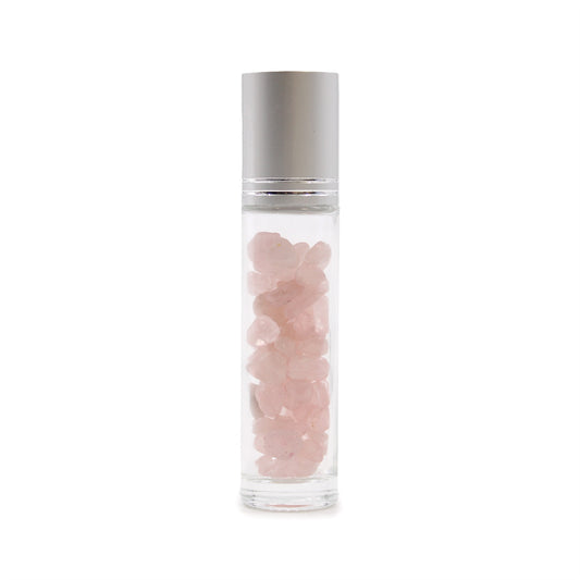 A glass rollerball bottle with a silver lid is standing. Inside, pink crystal chunks fill the space. The background is plain white.