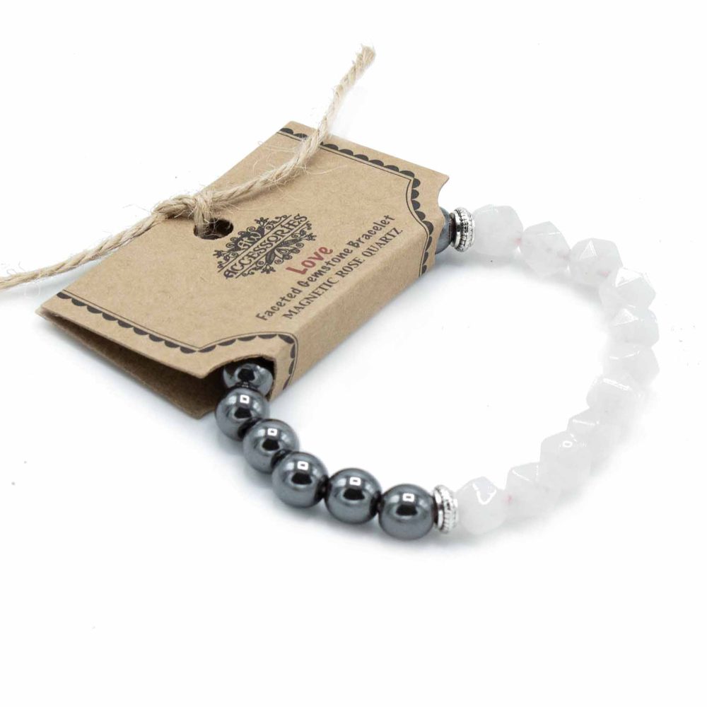 A beaded bracelet is packaged with a brown tag that reads, "Accessories Love Faceted Gemstone Bracelet MAGNETIC ROSE QUARTZ," on a white surface. The bracelet is partly hematite and partly white rose quartz.